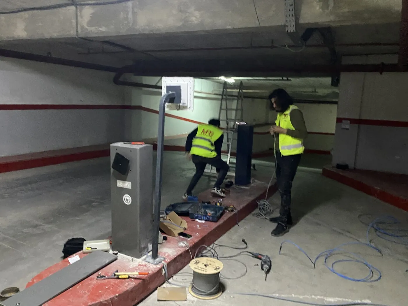 Techniciens MPS en gilet installant une barrière, une borne et des lecteurs dans un parking souterrain