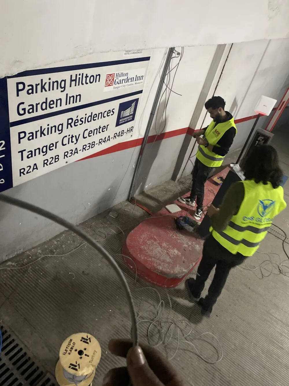 Techniciens en gilet installant des bornes et un lecteur dans un parking d’hôtel et de résidences